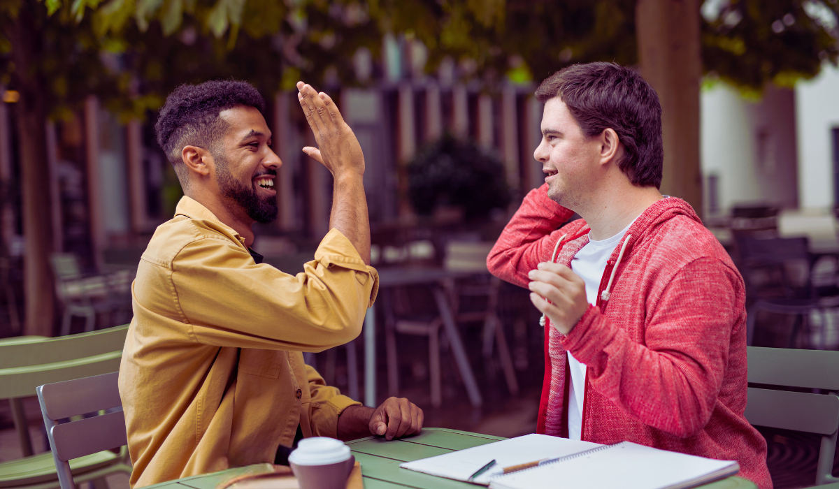 two adults hi-fiving, sitting at a table with some paperwork