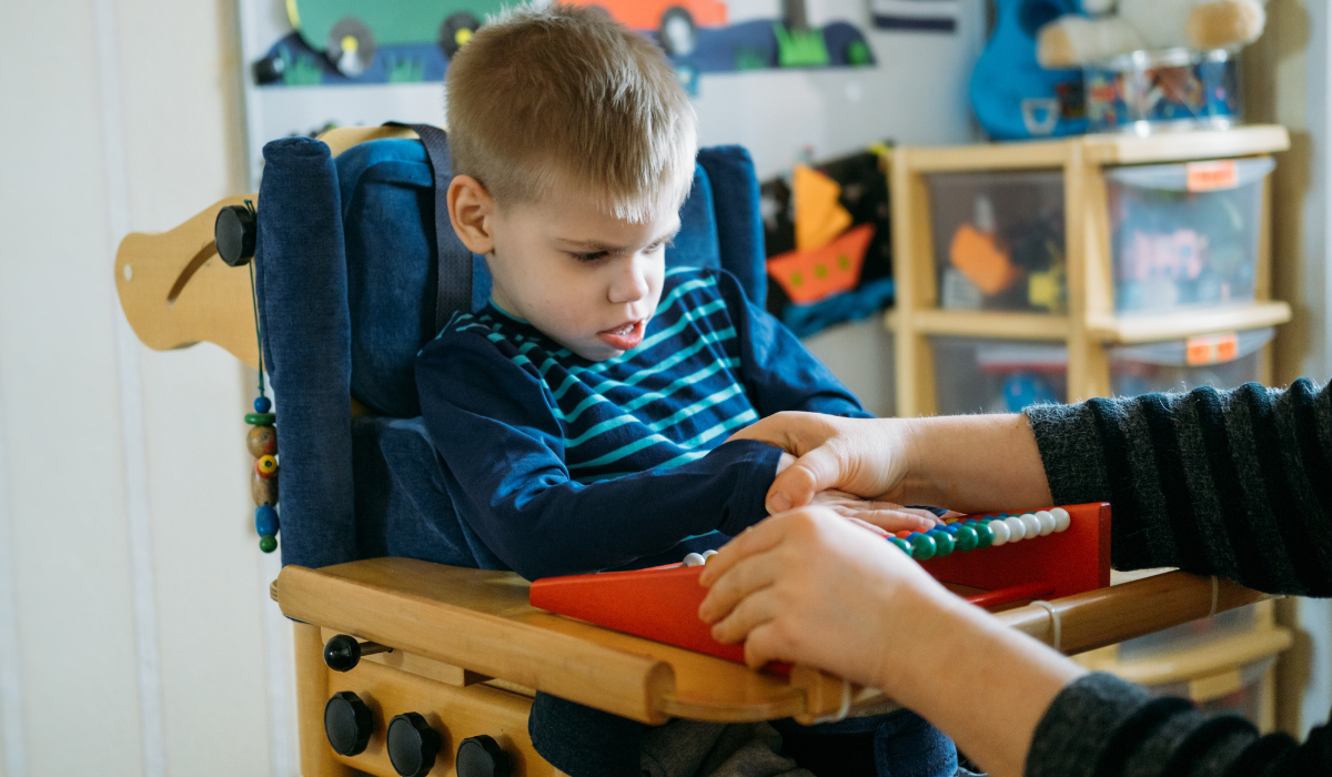 young boy in supported seating with teacher handling manipulatives