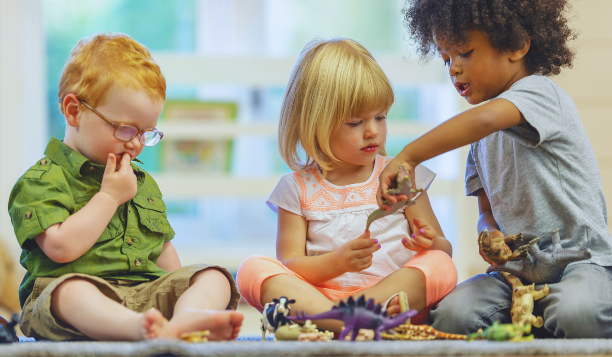 three young children sharing dinosaur toys