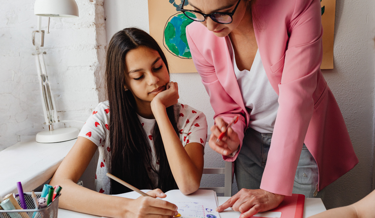 student working on a notebook with a teacher with a red pen giving feedback