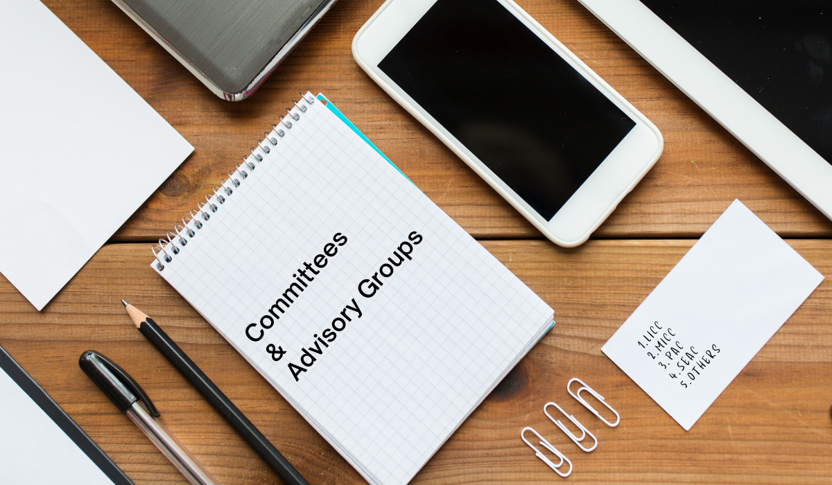 photo of a desk with a notepad and pen, text reads Committees and Advisory Groups