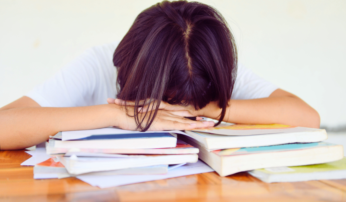 student with head down on stacks of books