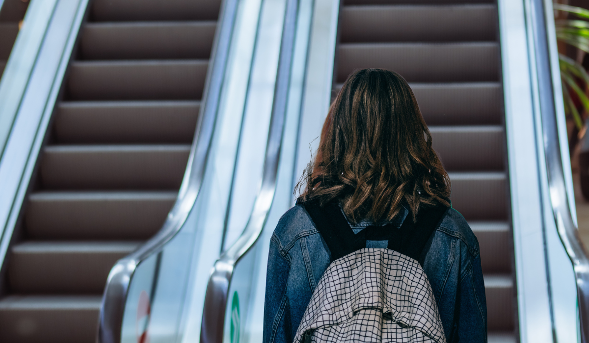 girl standing in front of escalator wearing a backpack